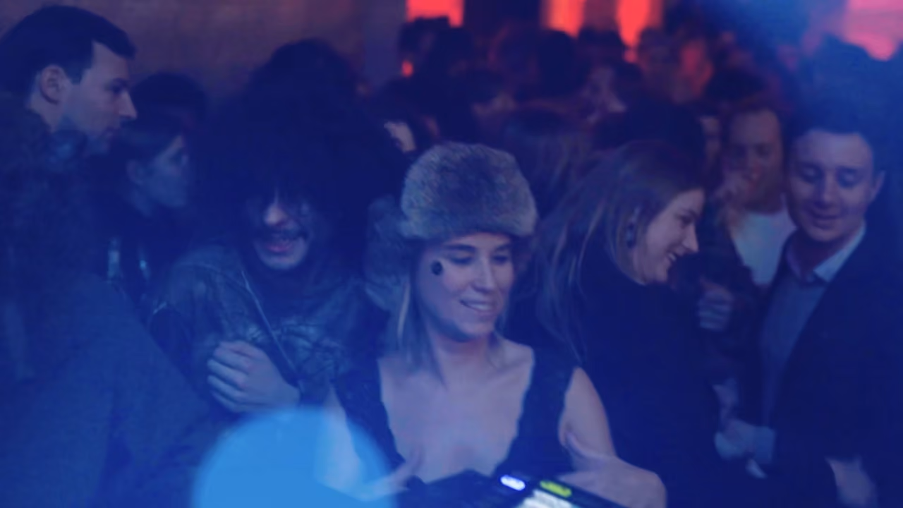 Foule en fête sous des lumières bleues lors de La Fête de l'Ours, une invitée en chapka au centre